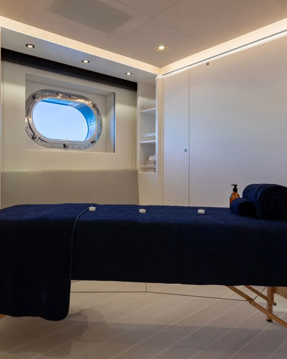 A massage table dressed in navy towels beneath a round porthole