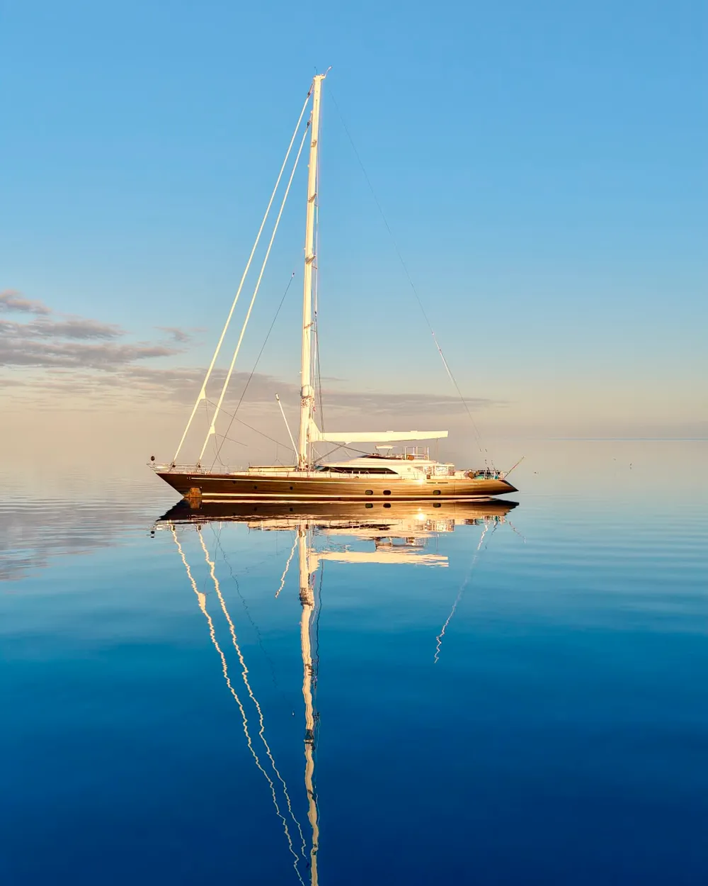 Serendipity I at anchor on glassy calm water, her mast perfectly reflected at sunrise