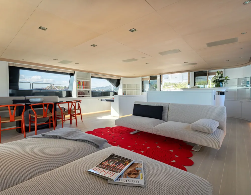 The bright main saloon with white sofas, a red rug and panoramic windows