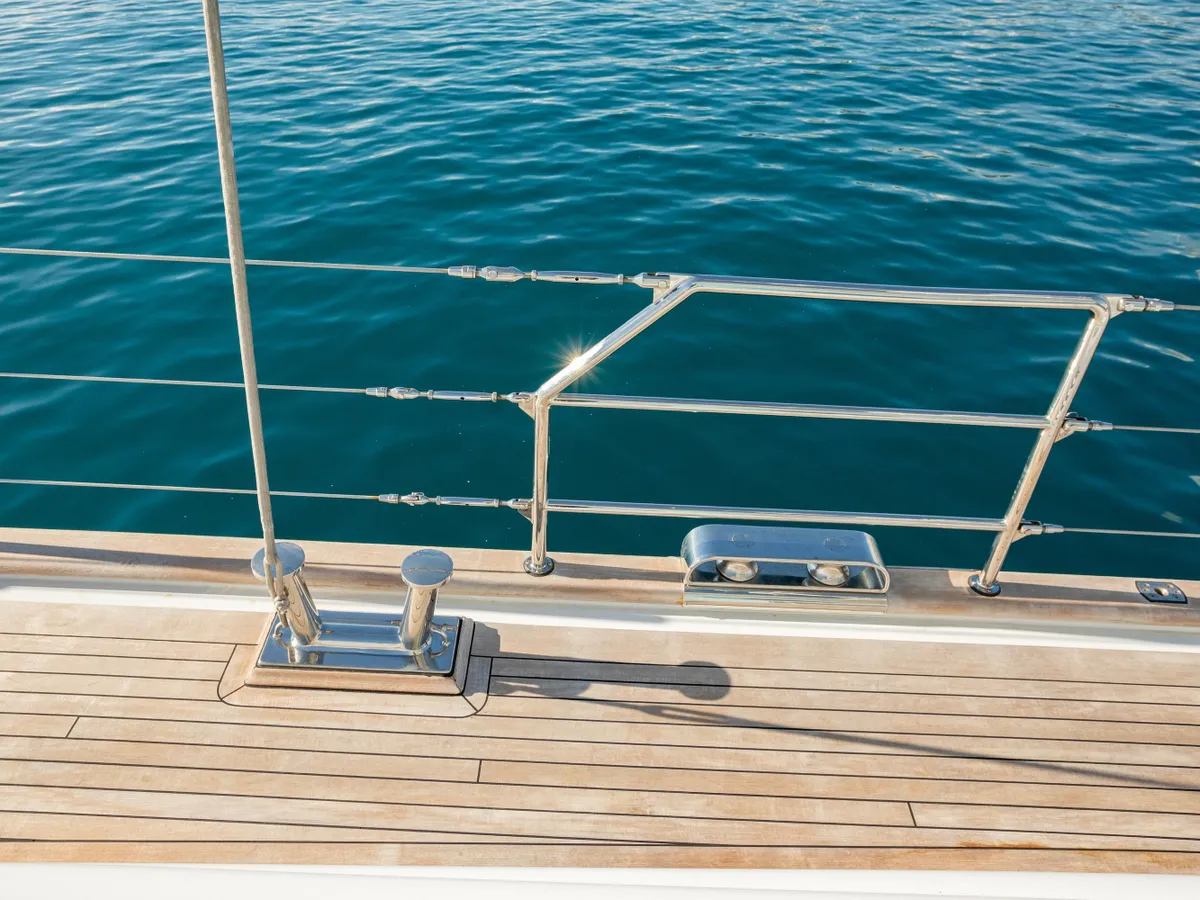 A polished deck railing above sunlit teak and deep turquoise water