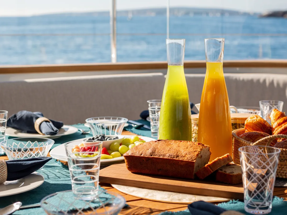 Bottled fresh juices, bread and fruit laid out on the aft deck with the sea beyond
