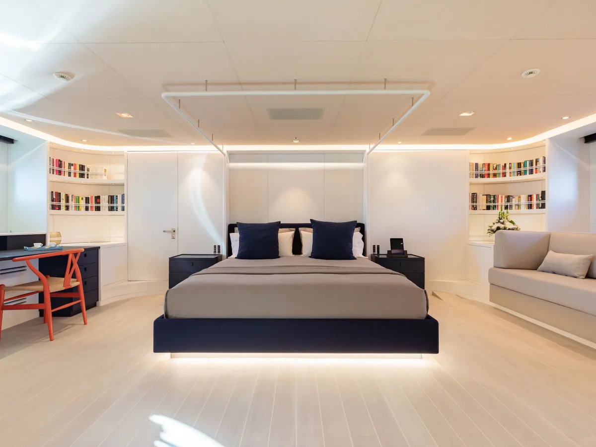 A double bed framed by white cabinetry and a curved sofa in the principal cabin