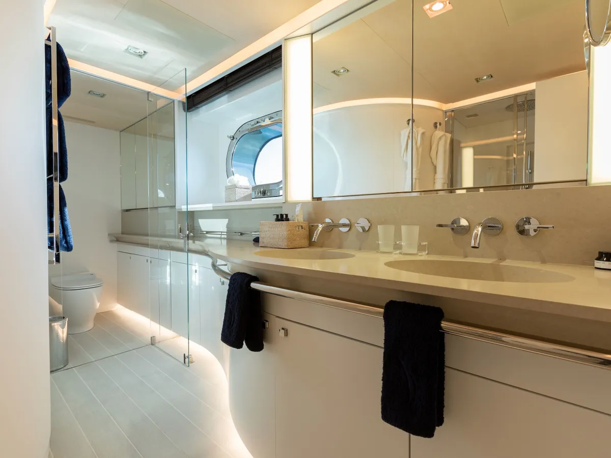 A bright en suite bathroom with twin basins, a wide mirror and a sea-facing porthole