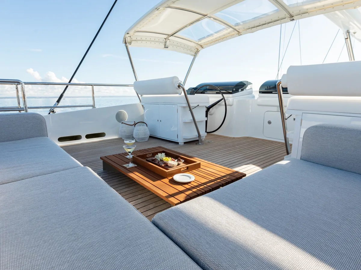 White cushioned seating and a teak coffee table beside the upper-deck helm