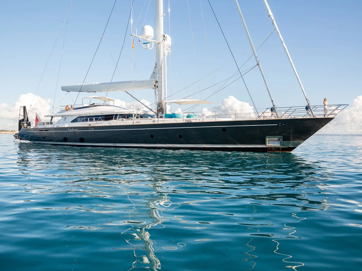 Side view of the yacht at anchor beside a sunlit coastline