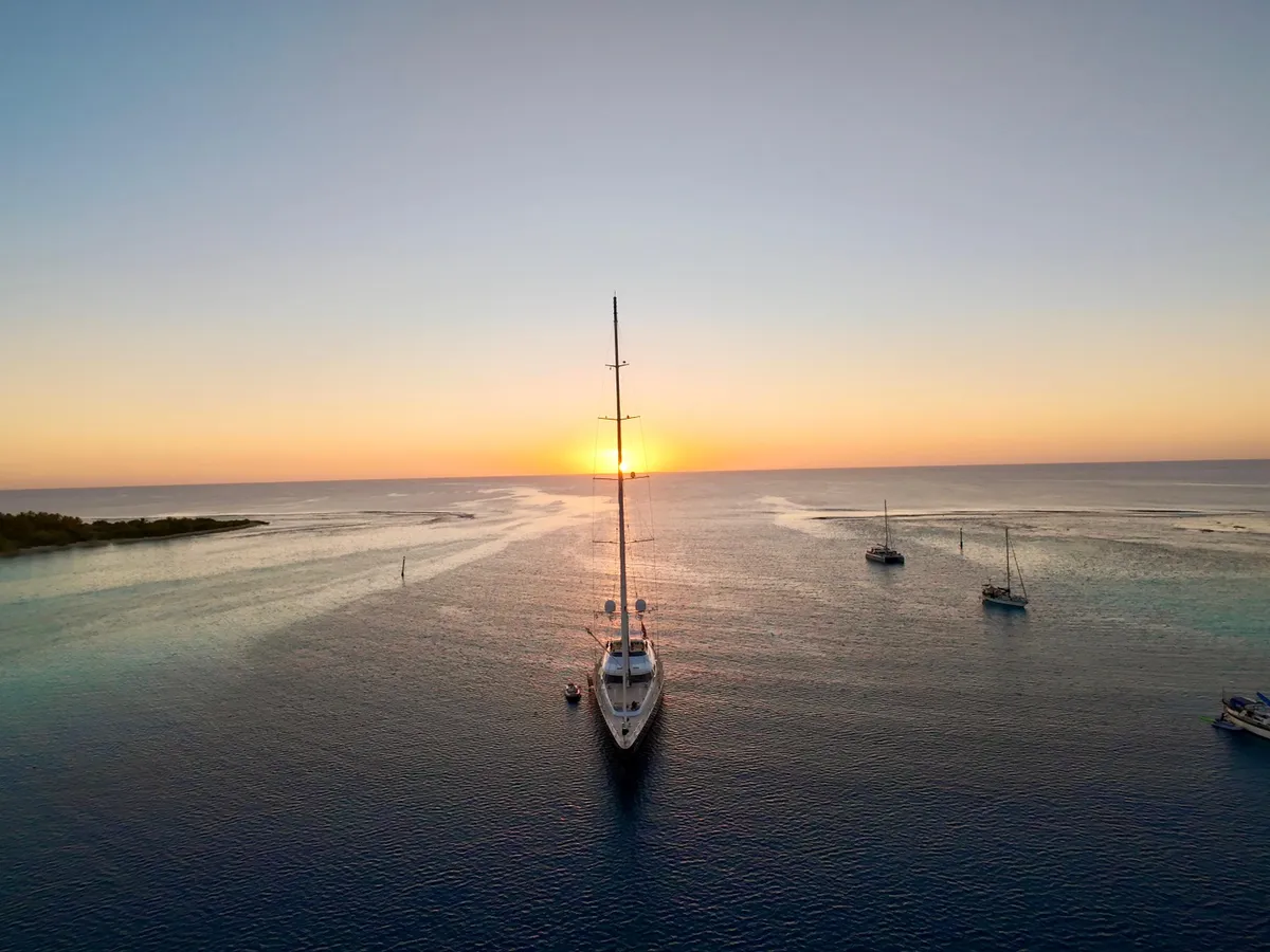 Serendipity I approaching a Polynesian atoll at sunset, bow-on with the sun low on the horizon