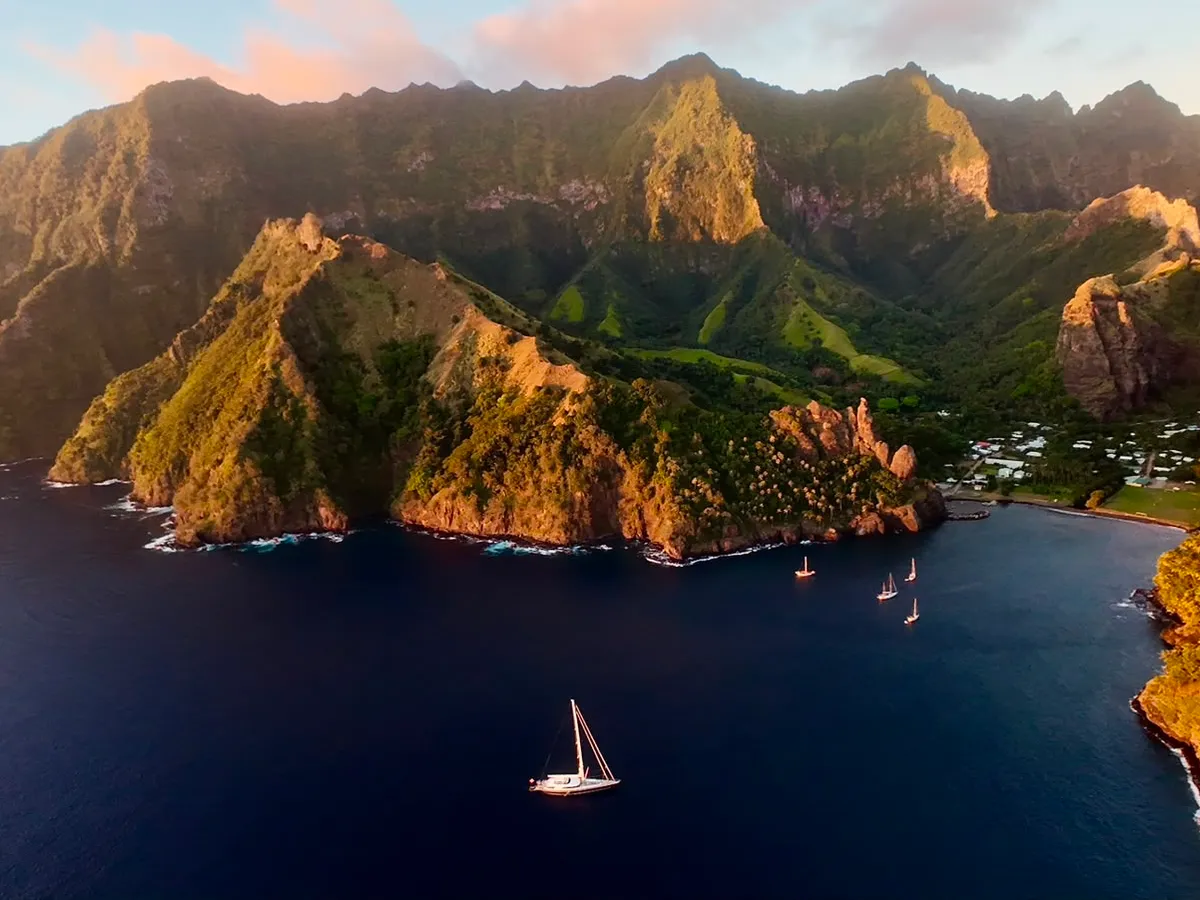 Serendipity I anchored in a bay beneath steep, forested Marquesas peaks at sunset with other yachts nearby