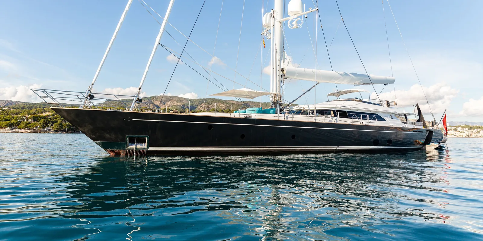 Dark blue two-masted sailing yacht at anchor with white sails up