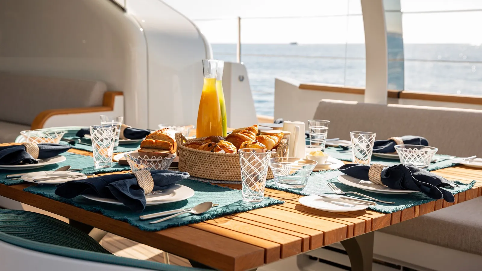 A breakfast table on the aft deck with fresh juices, bread and pastries, the sea beyond