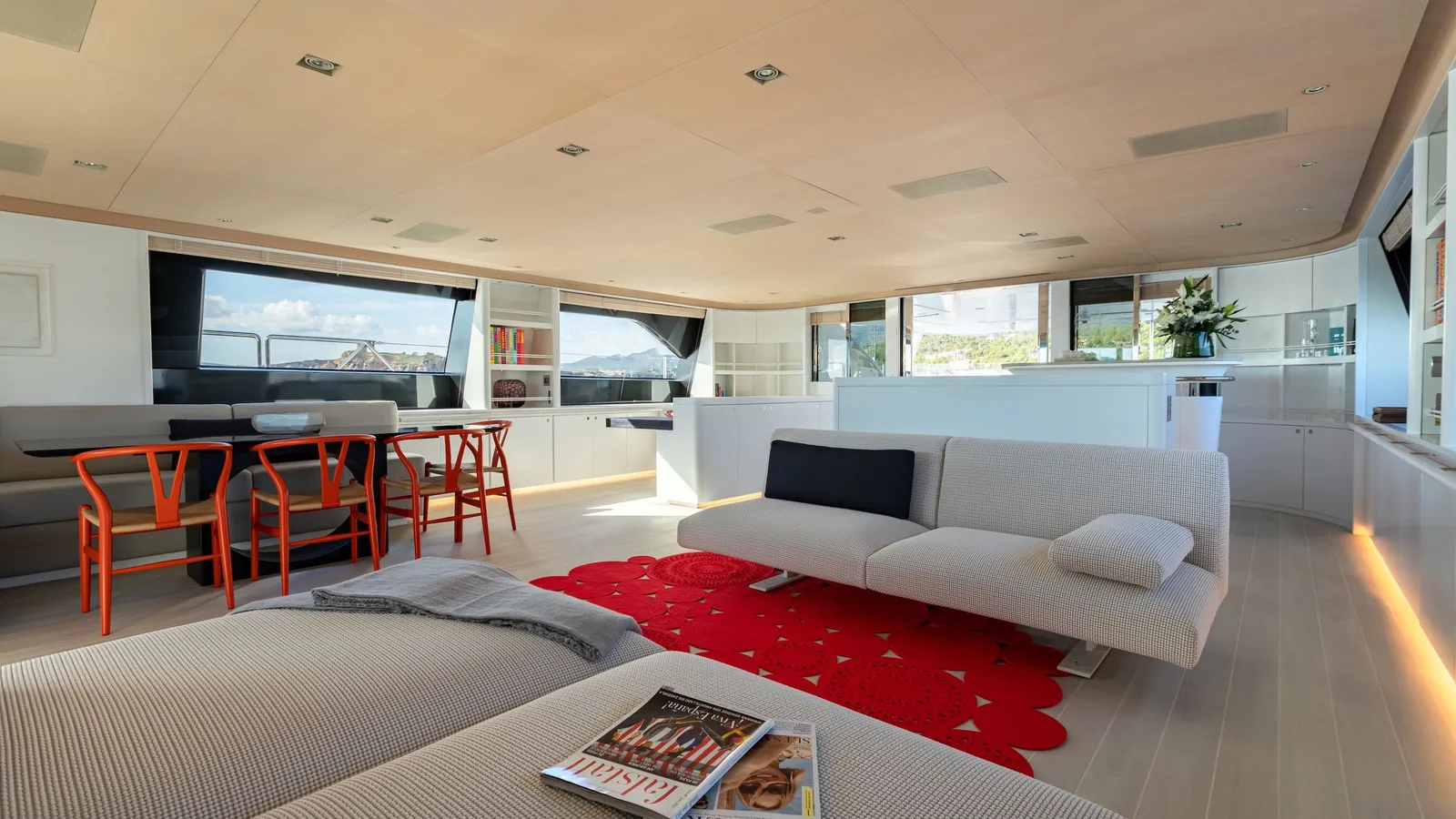 The bright main saloon with white sofas, a red rug and panoramic windows