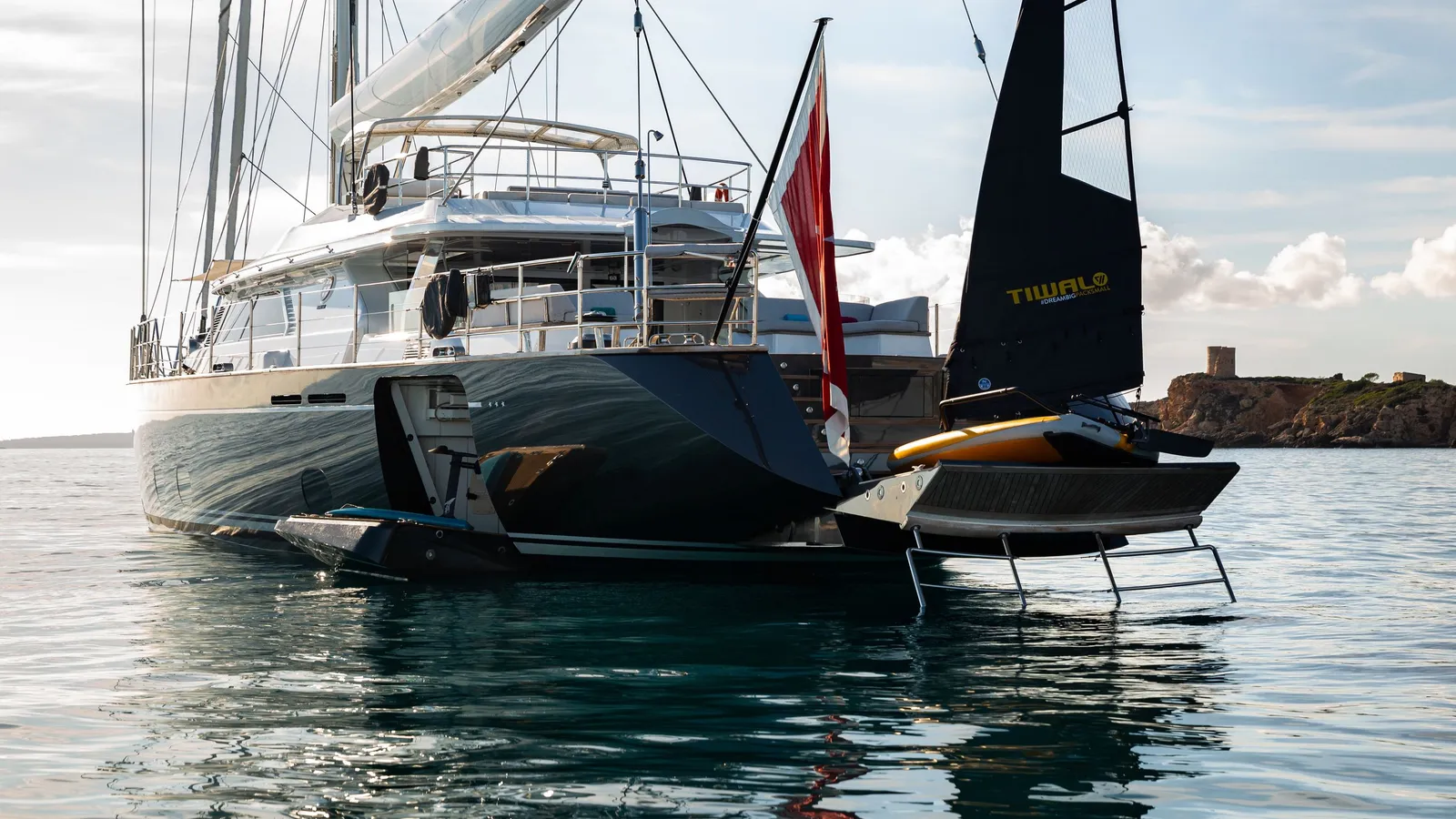 A Tiwal sailing dinghy on the water beside the stern of Serendipity I