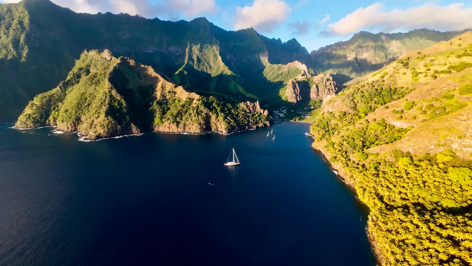 Serendipity I anchored in a deep blue Marquesas bay below volcanic cliffs