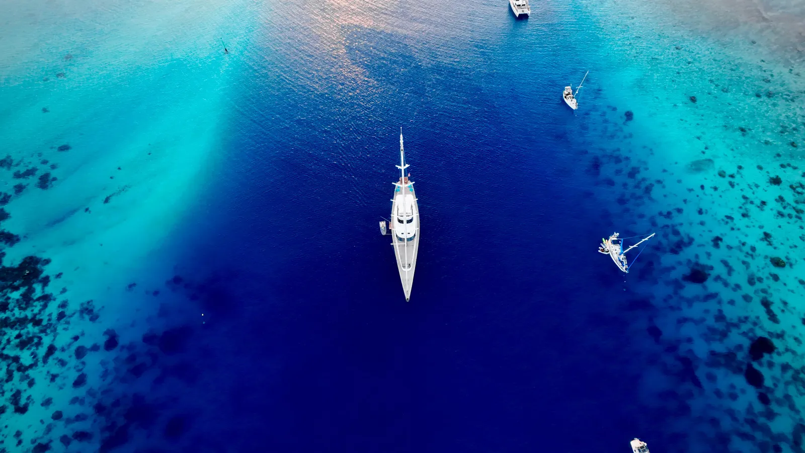 Aerial view straight down on Serendipity I anchored in a deep blue channel surrounded by reef and other yachts