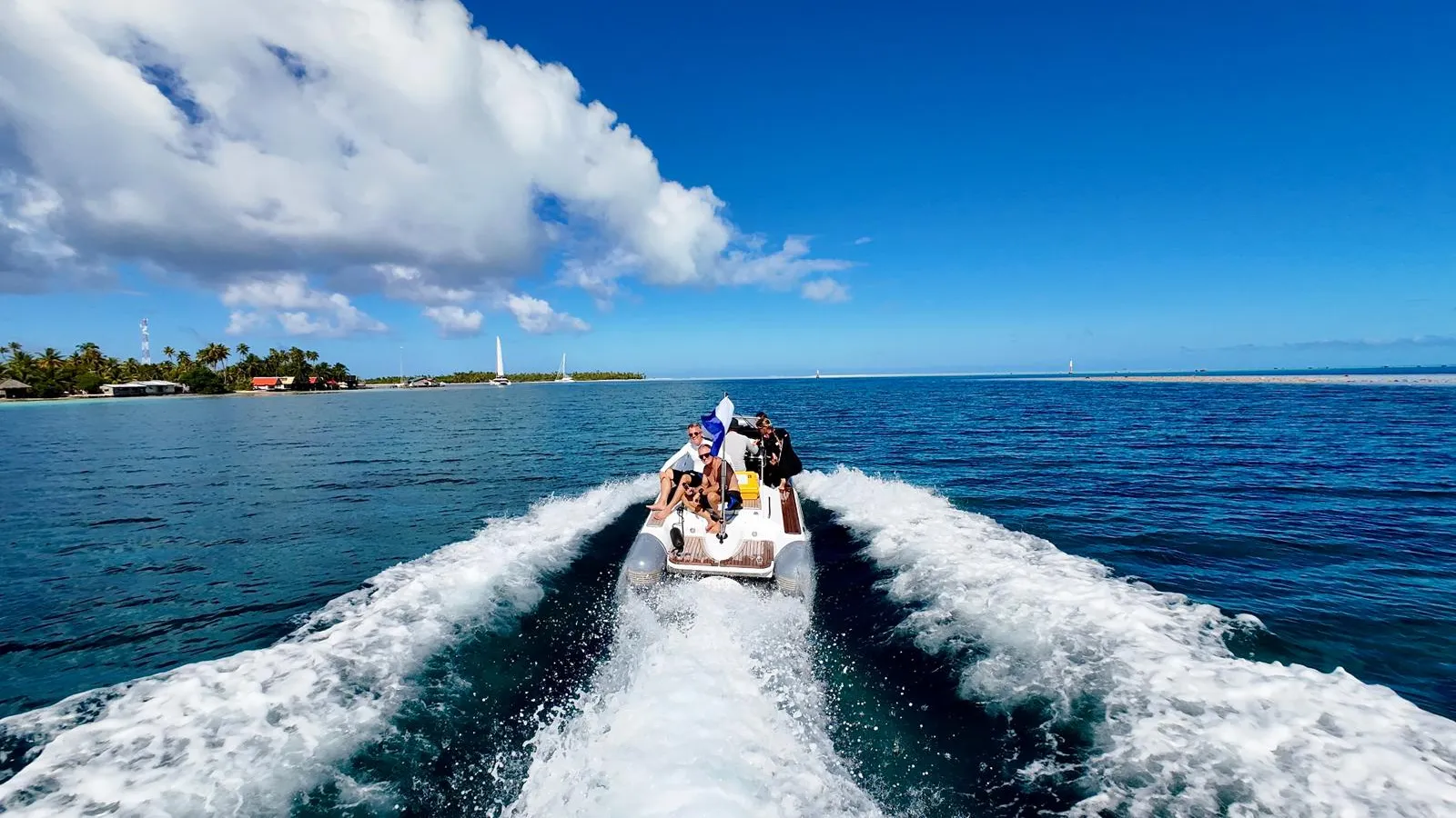 The RIB tender speeding across the lagoon with an island and reef beyond