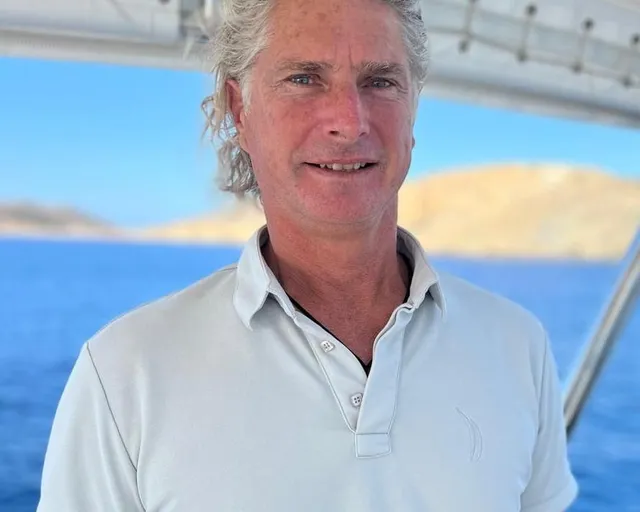 Senior crew member in white polo on deck overlooking calm blue water