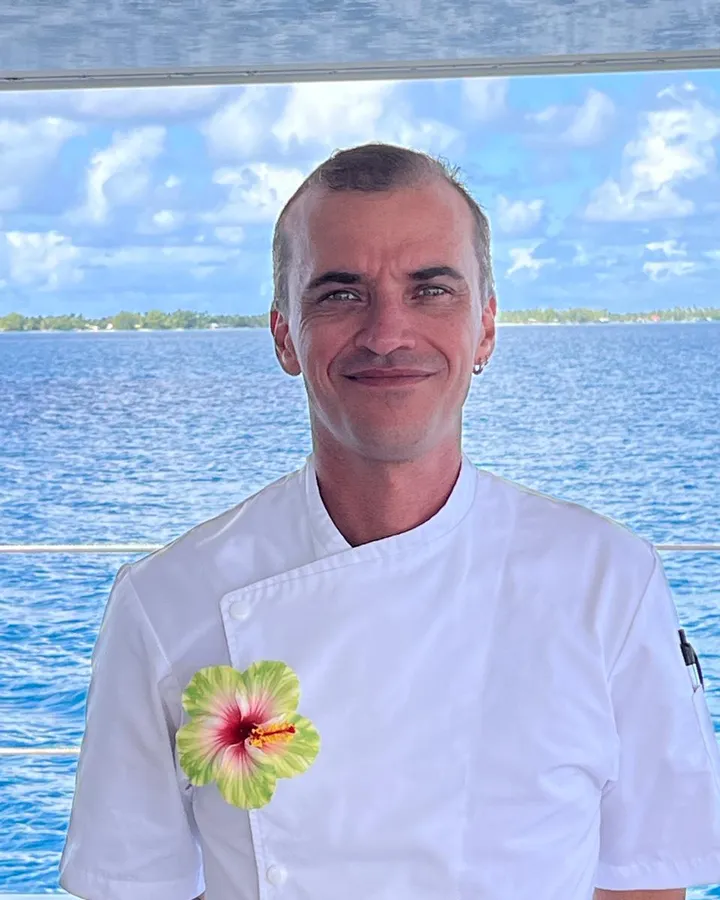 Chef Max in his white jacket on deck, a Polynesian lagoon behind him