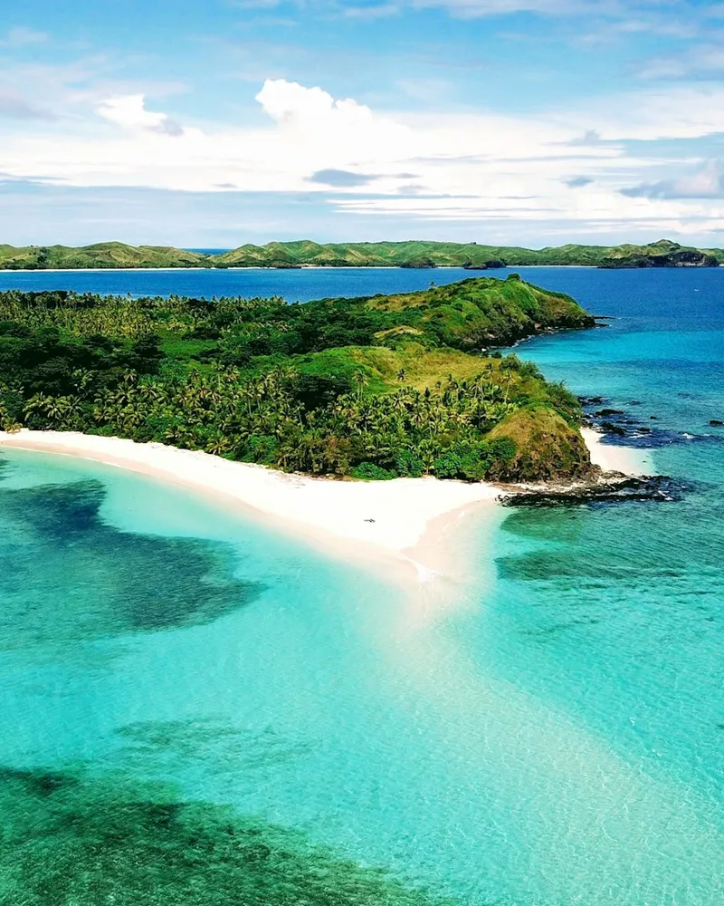 Aerial view of a palm-fringed sandbar island in a turquoise lagoon