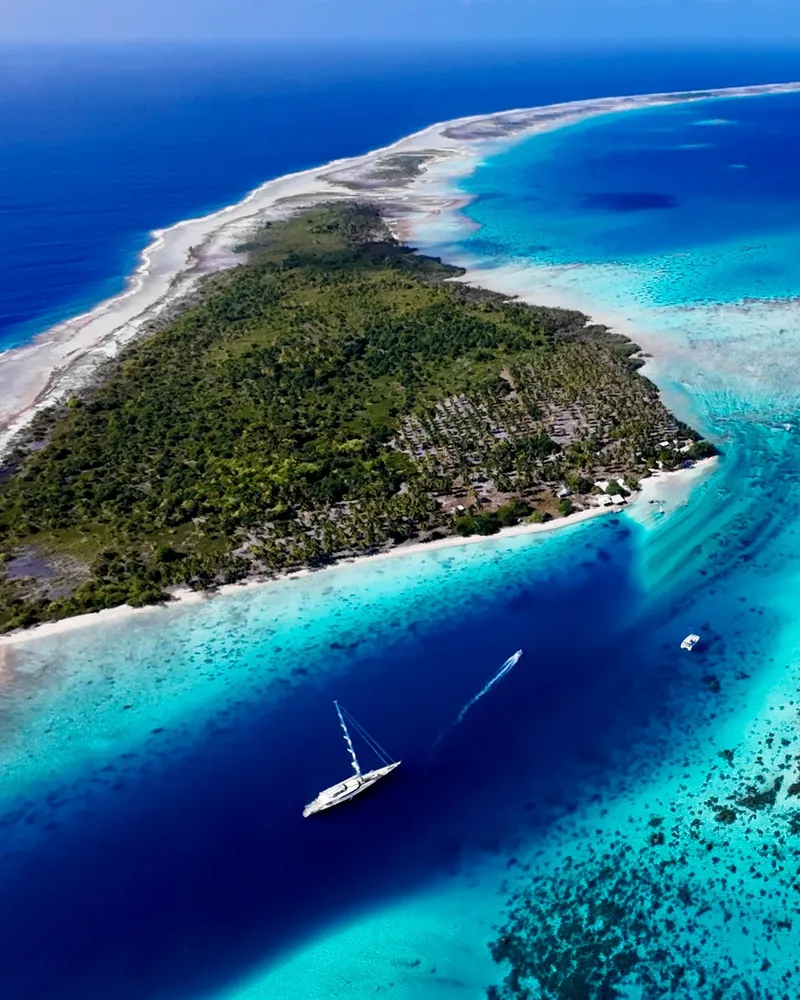 Aerial view of Serendipity I anchored beside a coral reef and a palm-covered motu