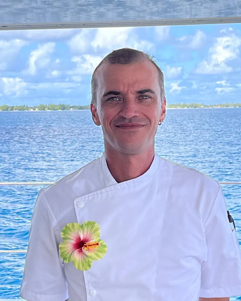 Chef Max in his white jacket on deck, a Polynesian lagoon behind him