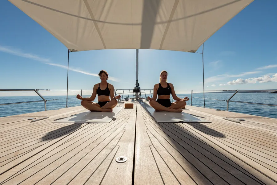 Two guests seated in meditation on the foredeck under the shade sail