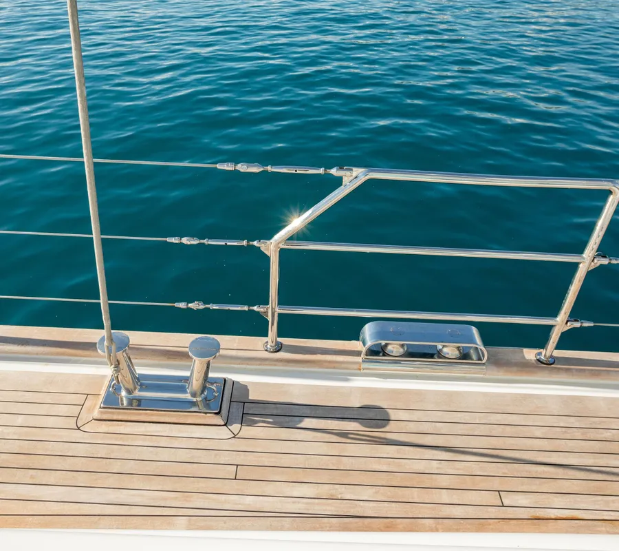 The teak deck and polished railing beside clear turquoise water