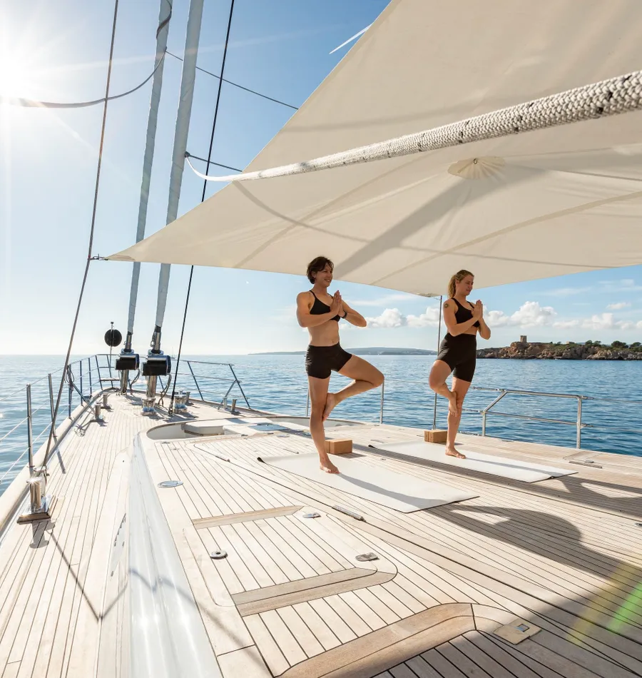 Two guests practising yoga on the teak deck beneath the sails