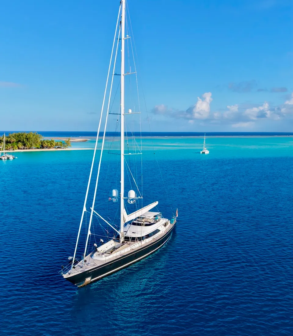 Serendipity I at anchor in a deep blue lagoon, a palm-fringed motu beyond