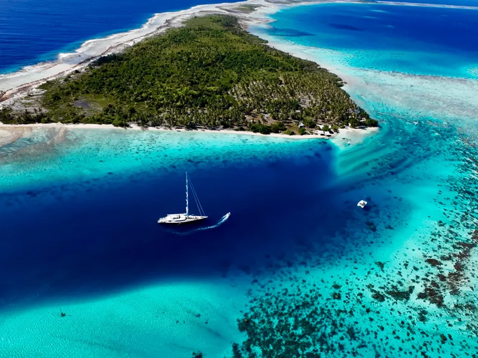 Serendipity I at anchor in deep blue water beside a reef-fringed Polynesian motu